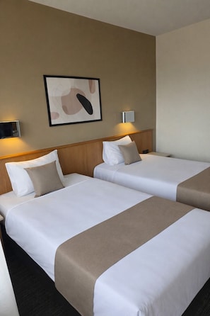 Habitación de hotel con dos camas, un cabecero, una lámpara de pared y una obra de arte abstracta enmarcada.