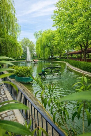 A serene park with a pond, a fountain, and a wooden gazebo.