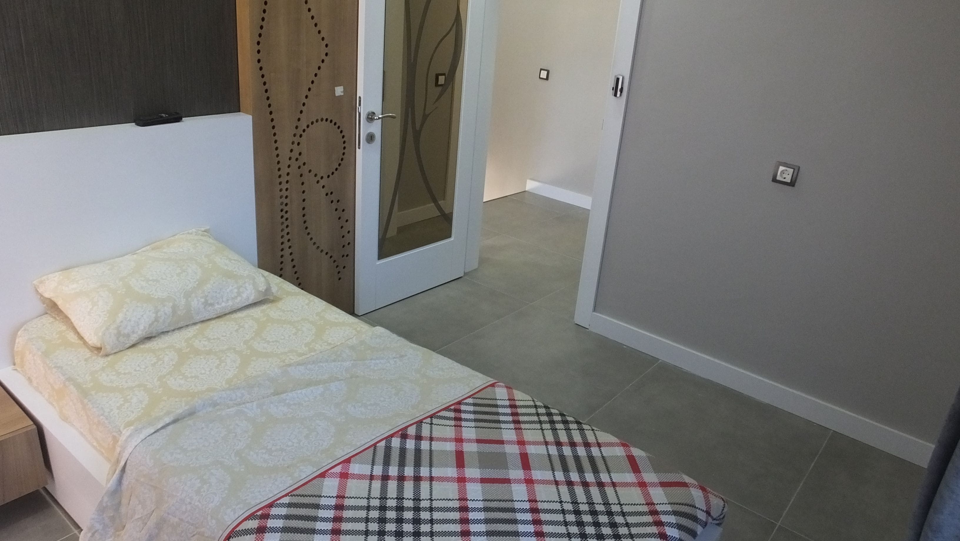 A bedroom with a bed, a wardrobe, and a door with a decorative pattern.
