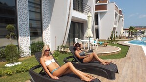 Two lounge chairs in a poolside area with a modern building in the background. - Han-De Homes (Kemer)
