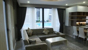 A modern living room with a sofa, coffee table, and dining area. - Han-De Homes (Kemer)