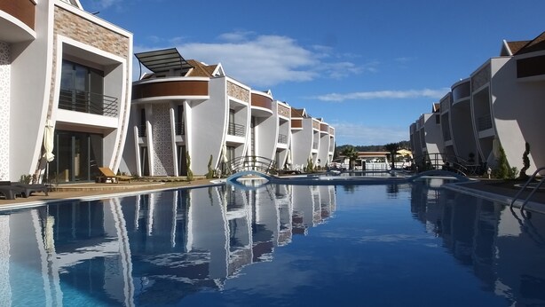A modern hotel with a central swimming pool, multiple balconies, and a clear blue sky. - Han-De Homes (Kemer)