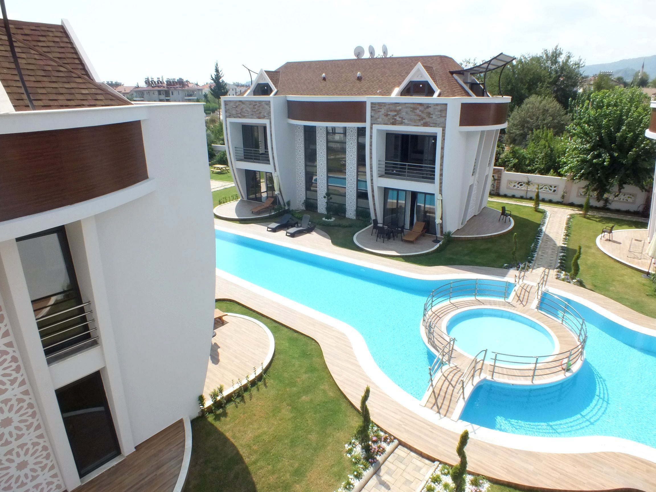 Ein modernes Gebäude mit einem Schwimmbad, einer überdachten Terrasse und einem angelegten Garten.