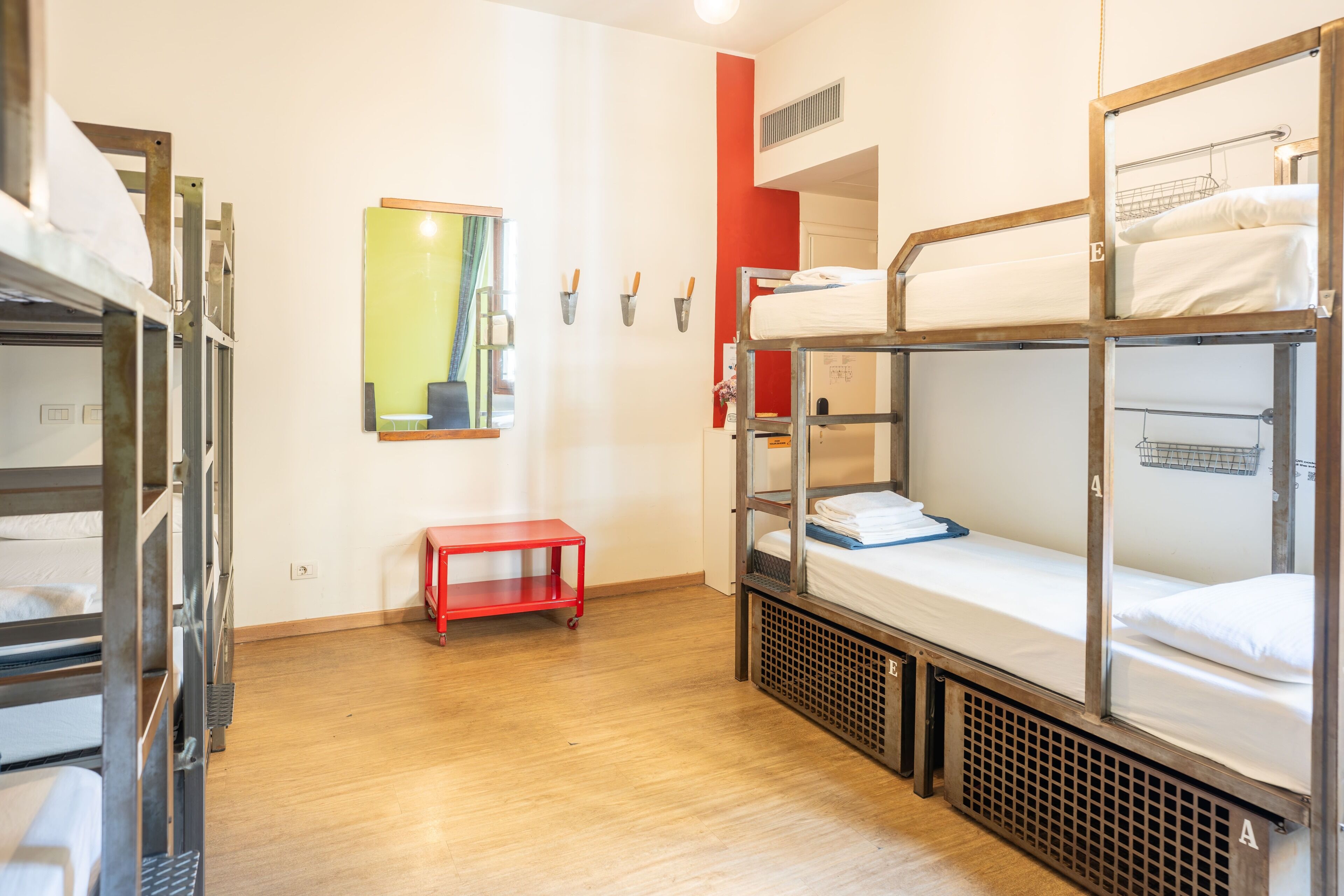 A dormitory room with bunk beds, a small red table, and a mirror on the wall.