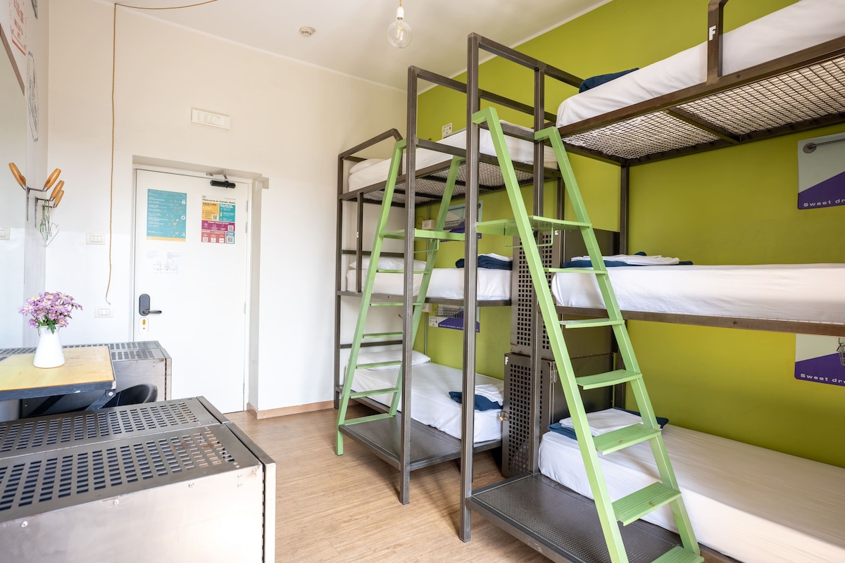 Habitación con literas, una escalera, un escritorio con un jarrón y una puerta con un aviso.