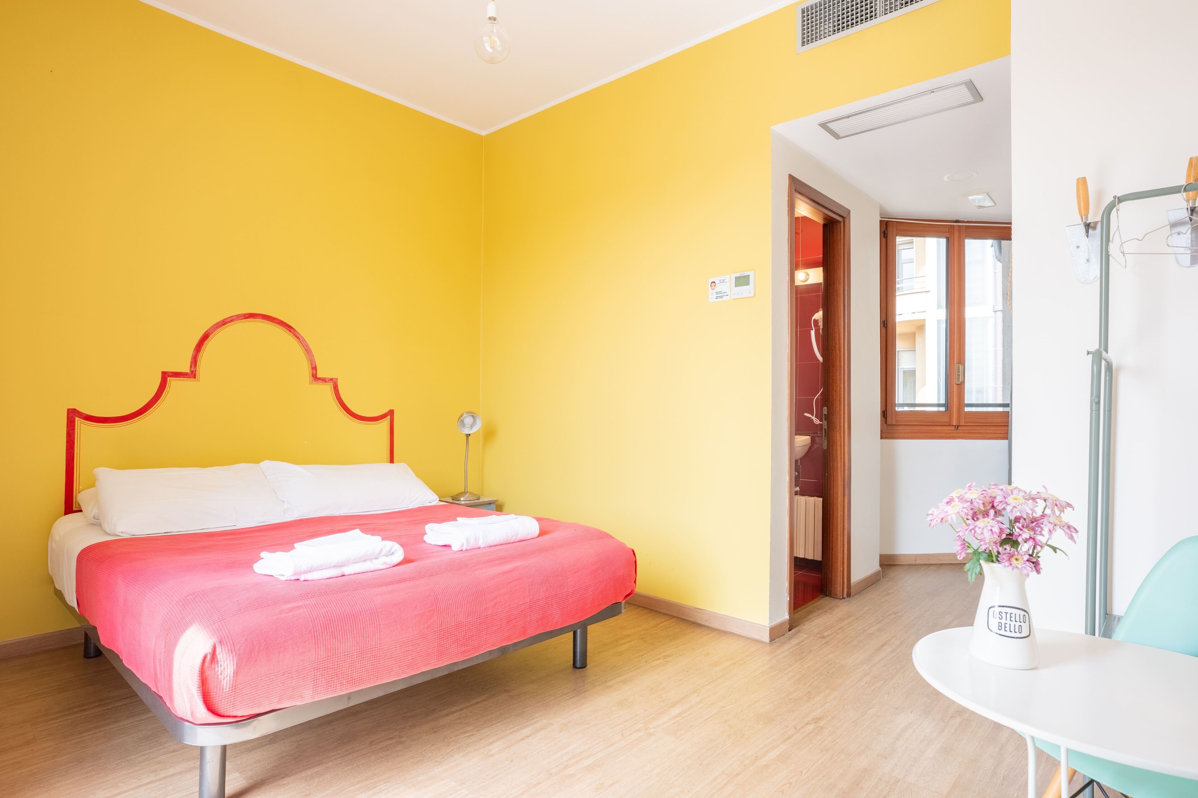 A room with a bed, a small table with a vase, and a door leading to another room.