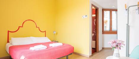 A room with a bed, a small table with a vase, and a door leading to another room.