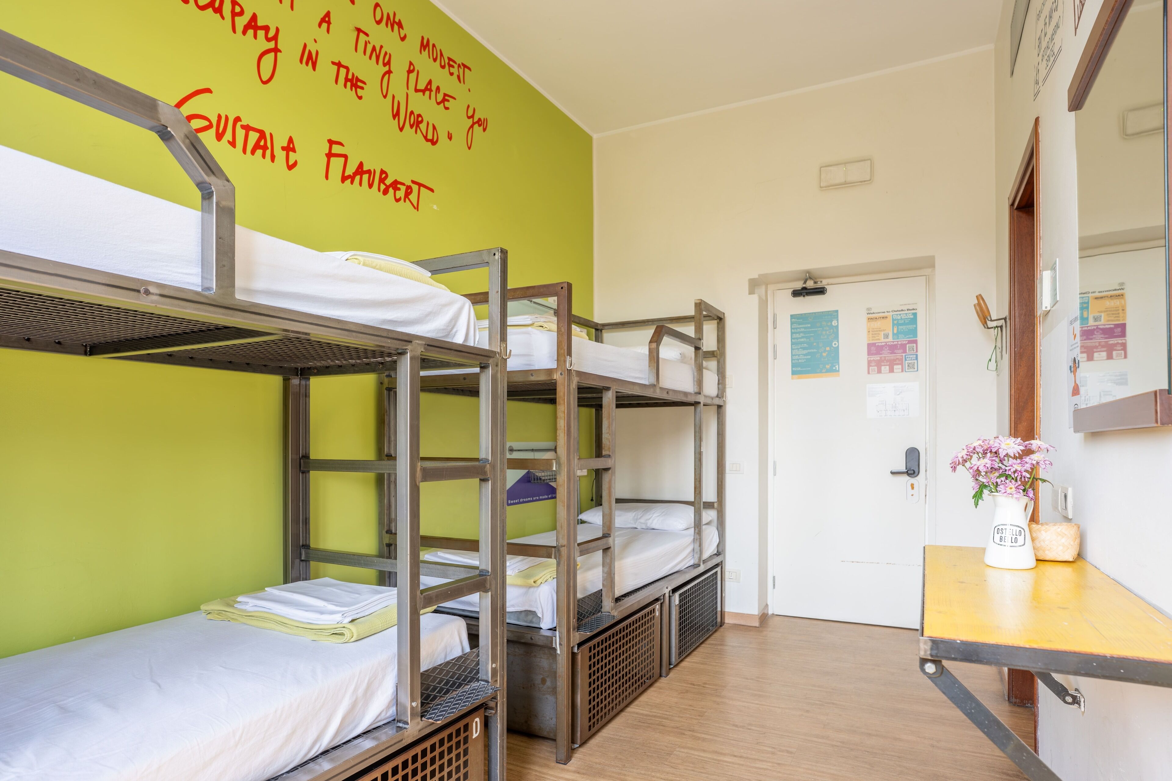 Camas literas en una habitación con pared verde y una puerta con un tablón de anuncios.