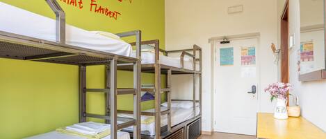 Camas literas en una habitación con pared verde y una puerta con un tablón de anuncios.