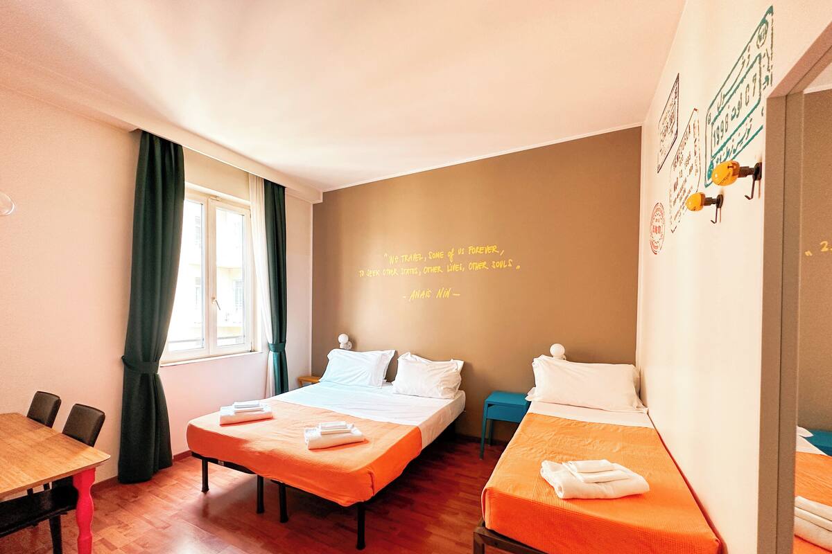 Habitación de hotel con dos camas, una mesa de comedor de madera y una pared con una cita.