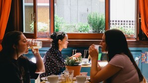 Un grupo de personas sentadas en una mesa con tazas y un vaso, en una habitación con ventana y plantas.