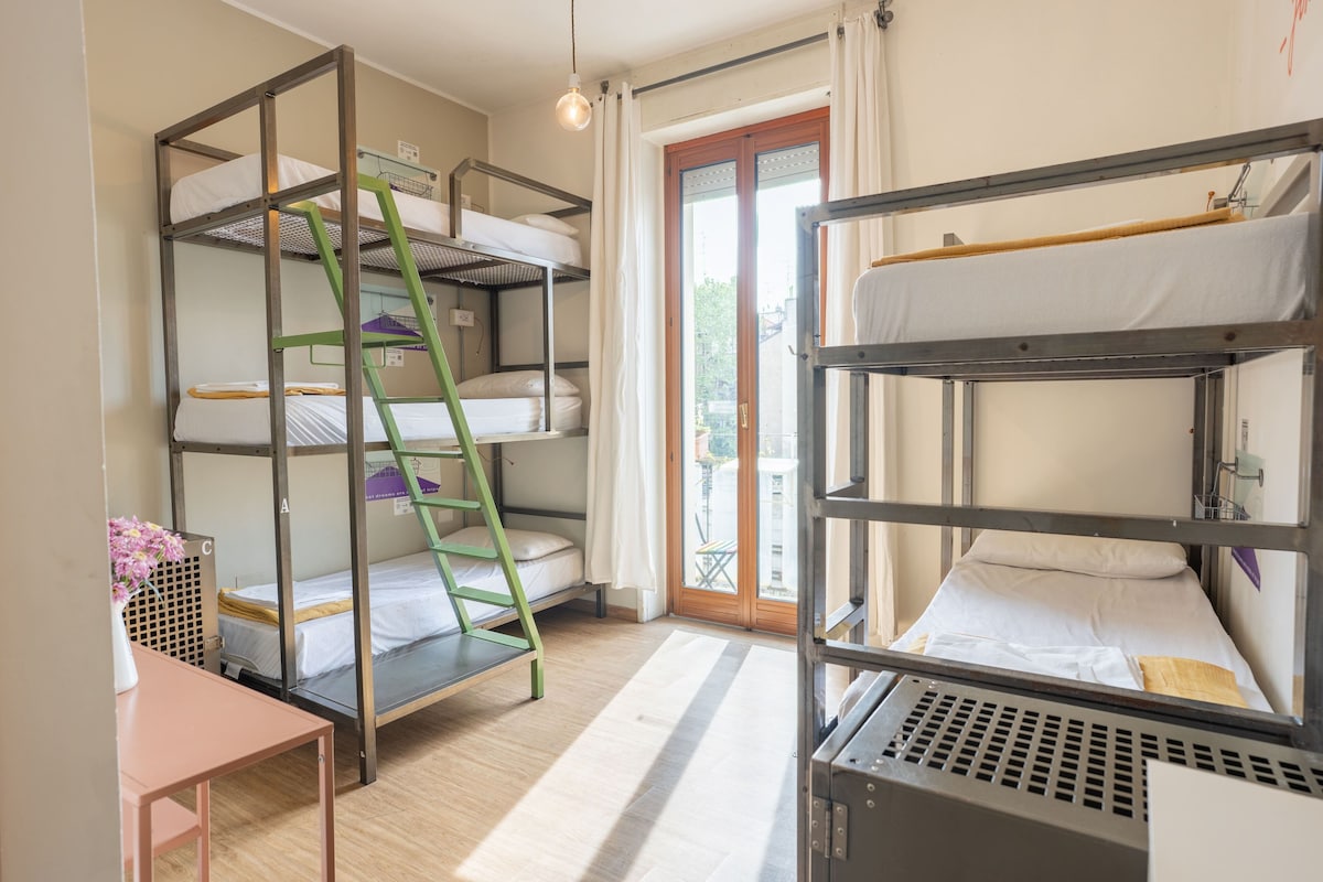 Un dormitorio con literas, escritorio, silla, escalera y ventana con cortinas.