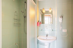 A bathroom with a glass shower enclosure, a white sink, and a hairdryer mounted on the wall.