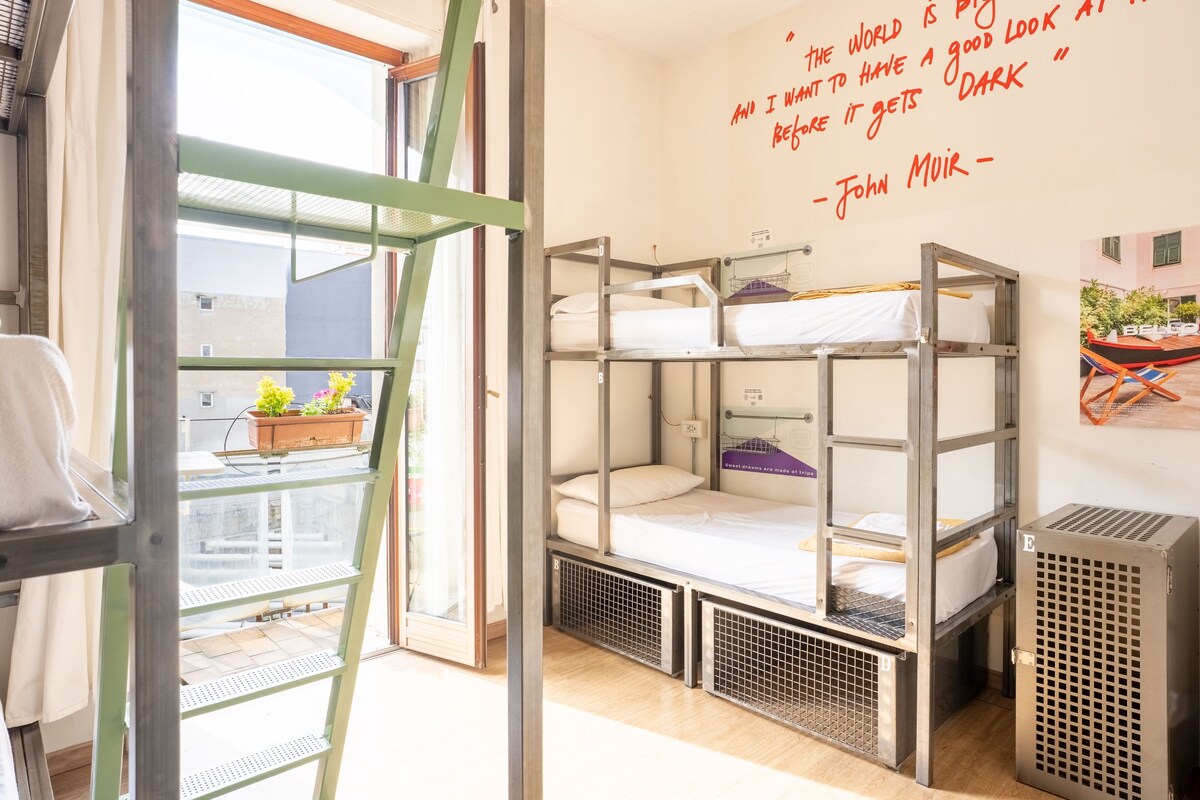 Habitación con literas, una ventana, una frase decorando la pared y un balcón pequeño con plantas.
