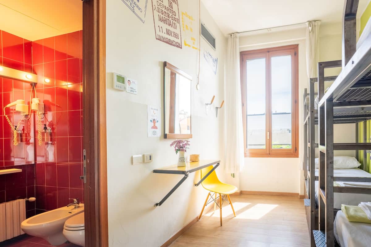 A hotel room with a red-tiled shower, a wooden bunk bed, a yellow chair, and a window with a view.