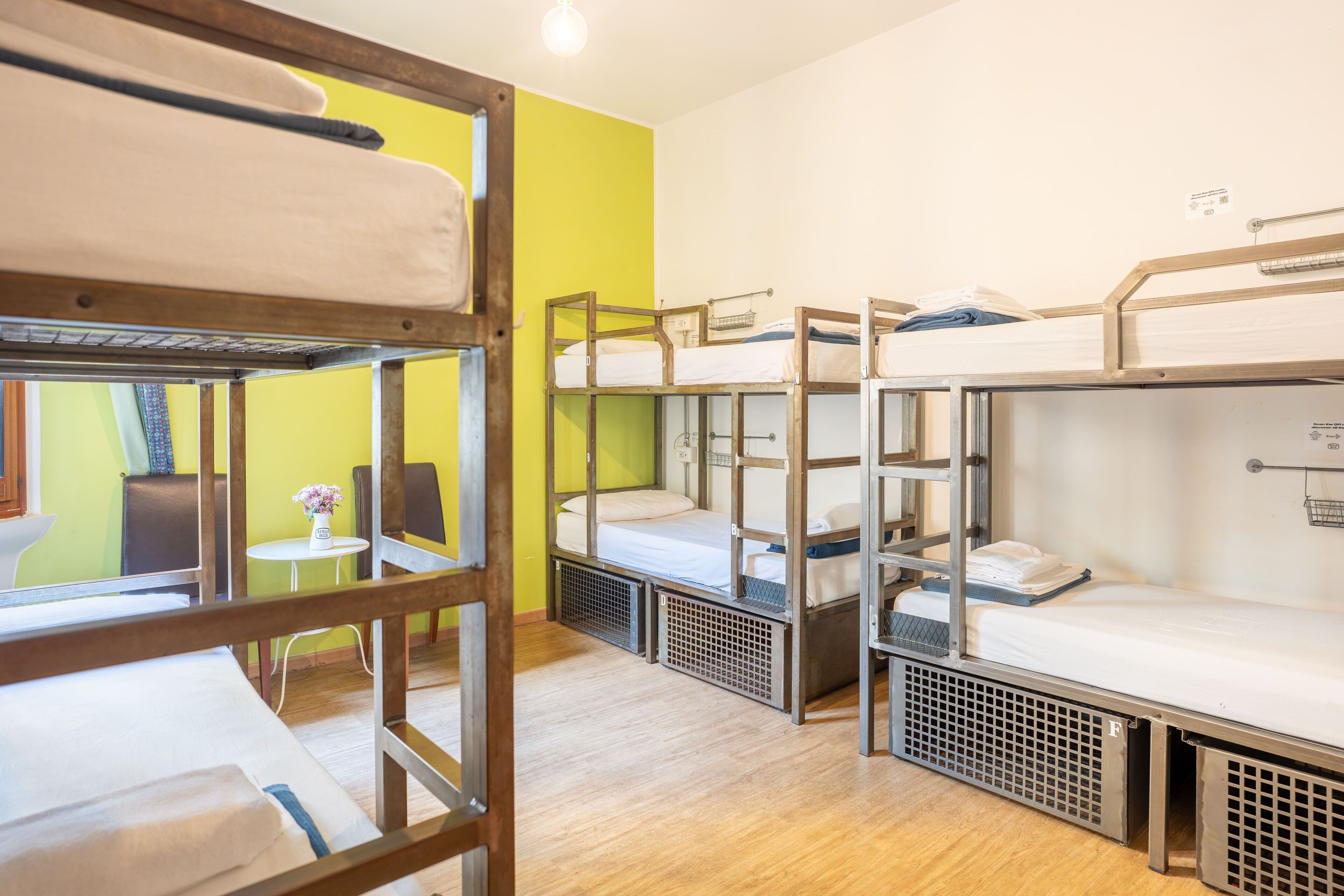 A dormitory room with bunk beds, a small table with a vase, and a chair.