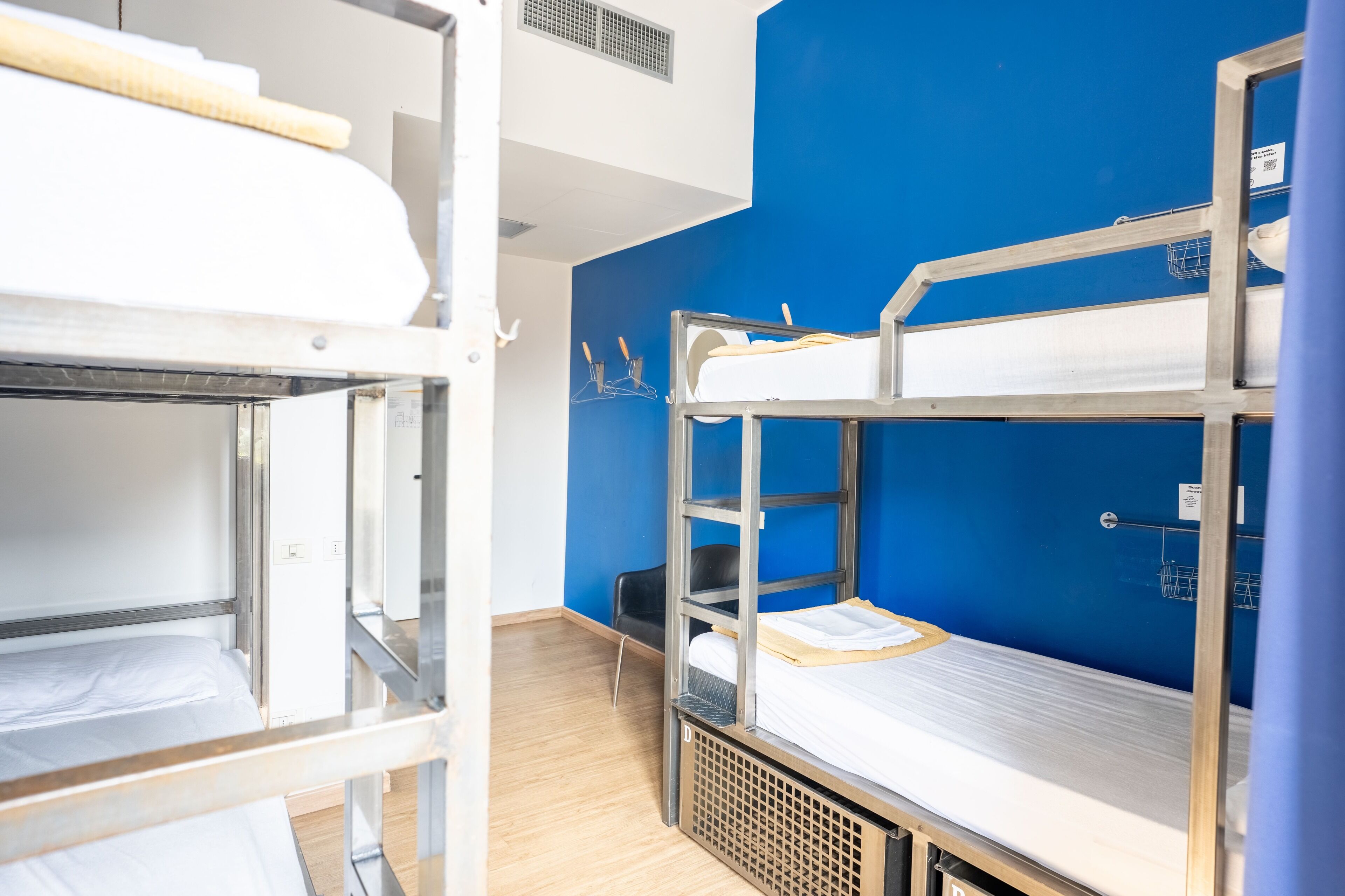 Ein Mehrbettzimmer mit blauer Wand, einem schwarzen Stuhl und einem Lüfter an der Decke.