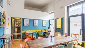 Una habitación con una mesa de madera, sillas coloridas, una persona trabajando en un ordenador portátil y una puerta que da a otra habitación.
