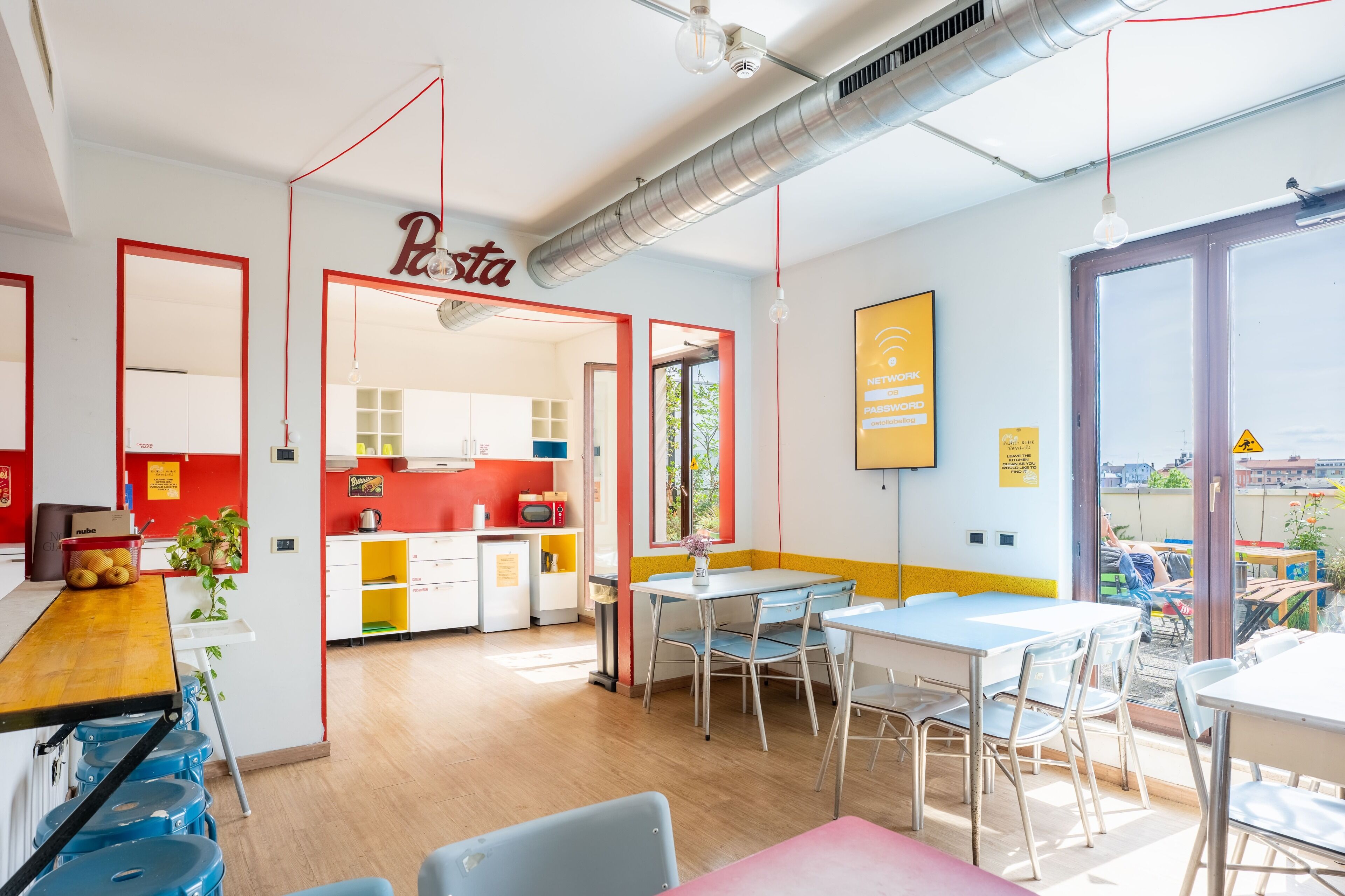 Una cocina moderna con detalles en rojo, un comedor con sillas azules y vistas amplias a través de grandes ventanales.