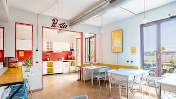 A modern kitchen with red accents, a dining area with blue chairs, and a view through large windows.