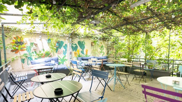 Un patio al aire libre con mesas y sillas, un mural y vistas a zonas verdes.