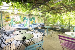 Un patio al aire libre con mesas y sillas, un mural y vistas a zonas verdes.