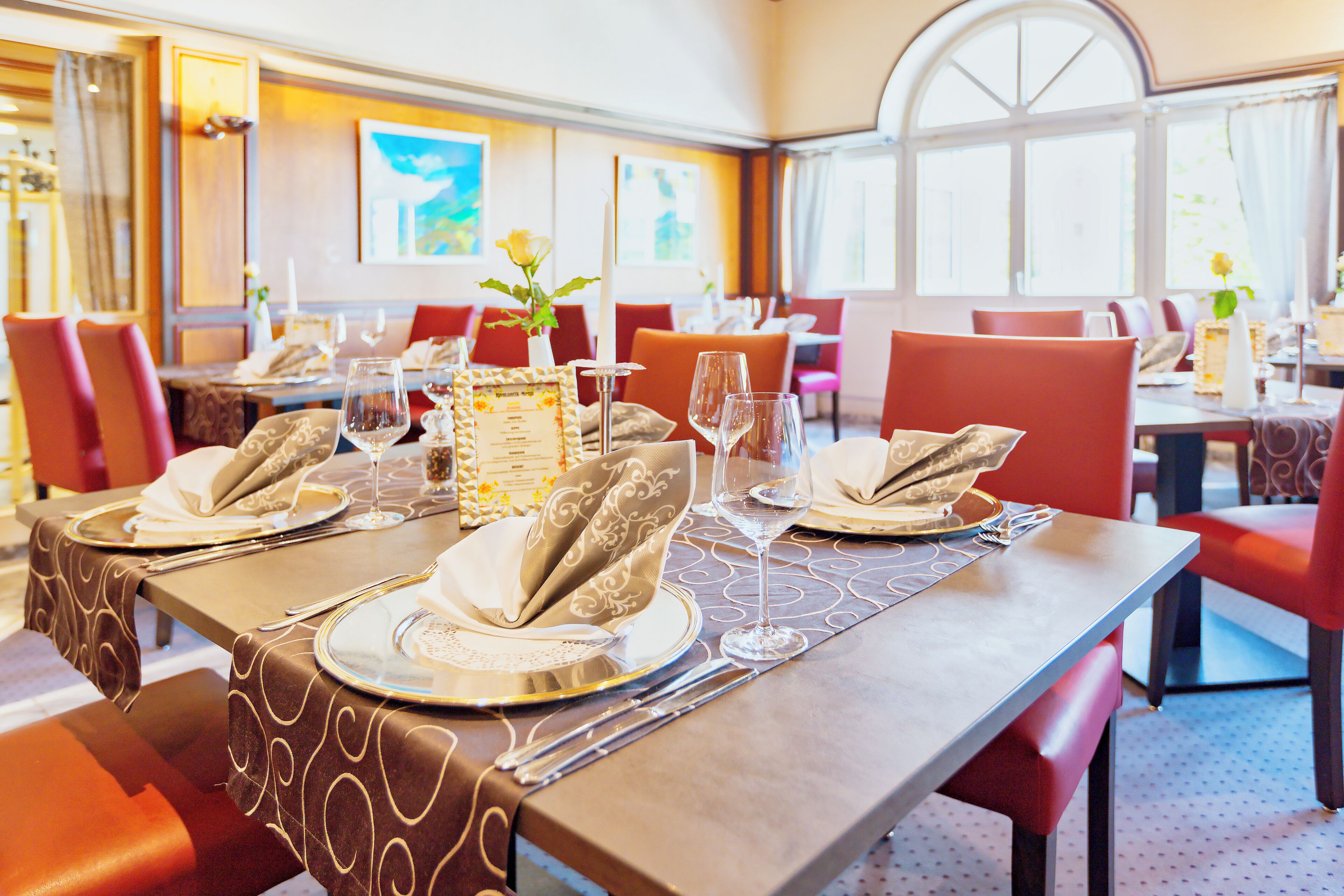 Ein Restaurant mit gedeckten Tischen, das modernes Design mit gemusterten Tischdecken und roten Stühlen aufweist.