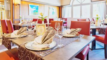 Ein Restaurant mit gedeckten Tischen, das modernes Design mit gemusterten Tischdecken und roten Stühlen aufweist.