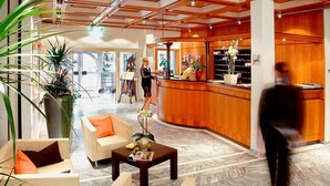 A hotel lobby with a reception desk, seating area, and a view of the outside. - Hotel Sonnengarten (Bad Woerishofen)