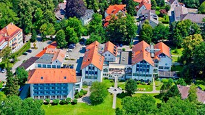 An aerial view of a residential area with multiple houses, a central building with a red roof, and a well-maintained lawn. - Hotel Sonnengarten (Bad Woerishofen)