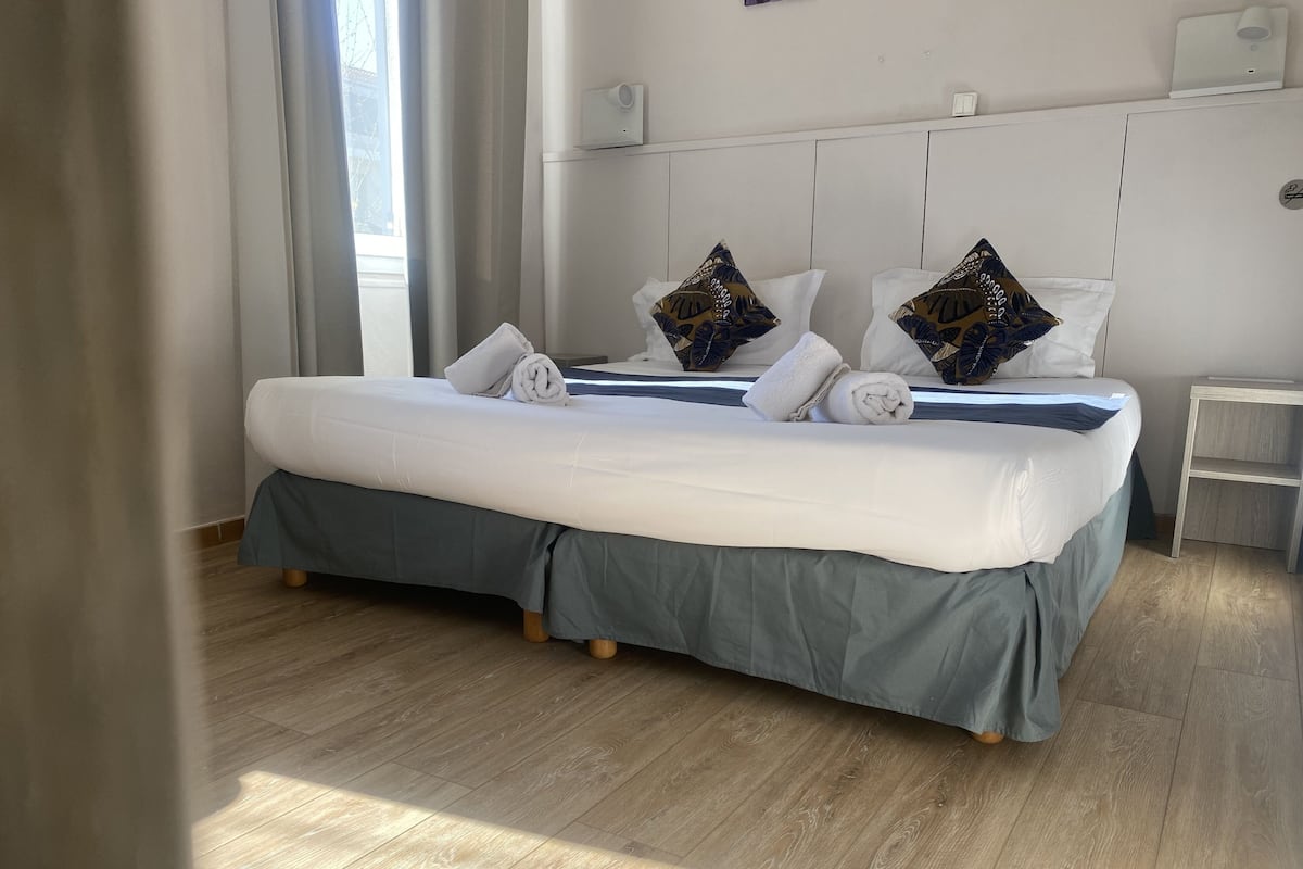 Un lit bien fait, avec une literie blanche et bleue, deux coussins décoratifs et un plancher en bois.
