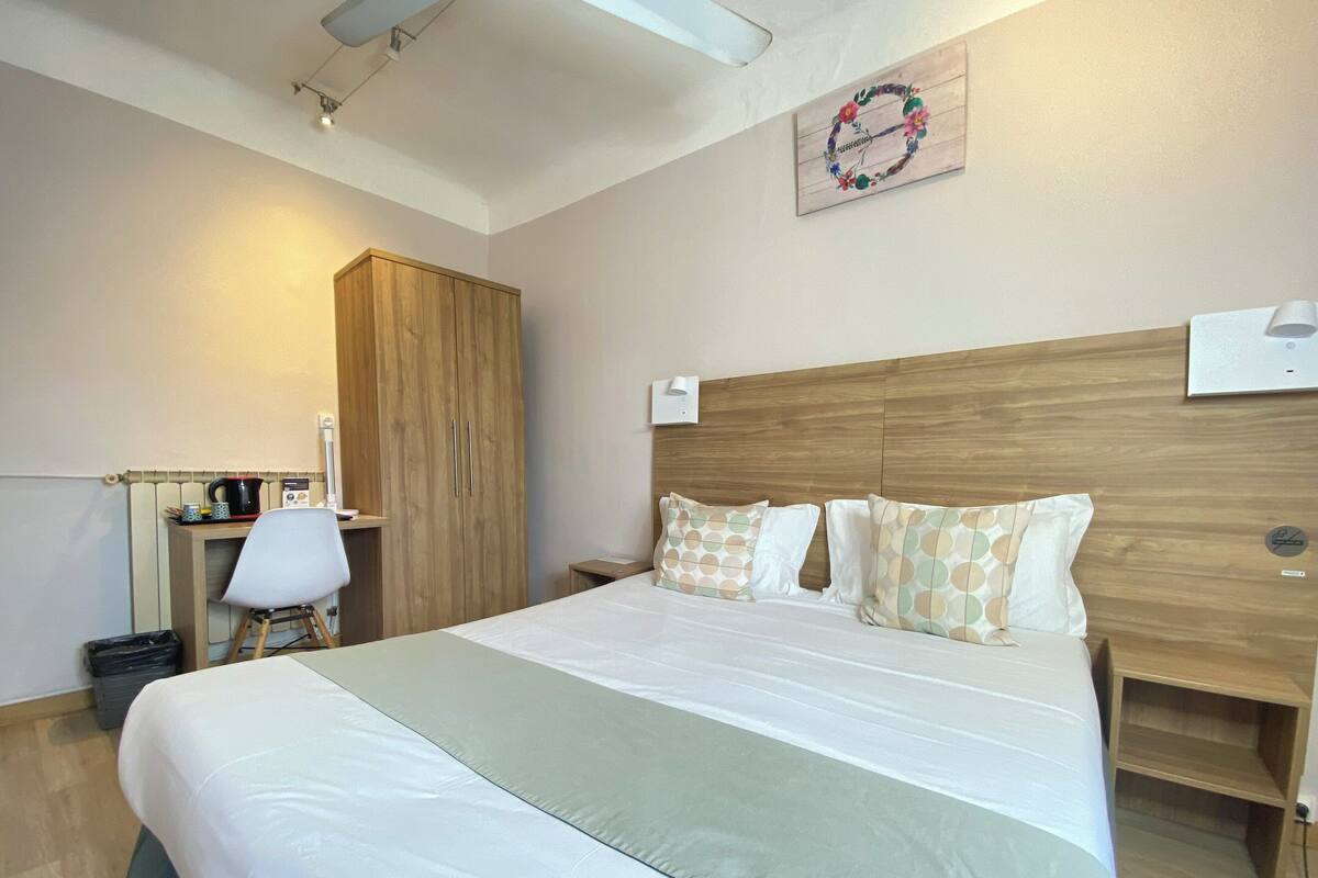 Une chambre d’hôtel bien aménagée, avec un grand lit, une armoire en bois, un bureau avec une chaise et un luminaire fixé au mur.