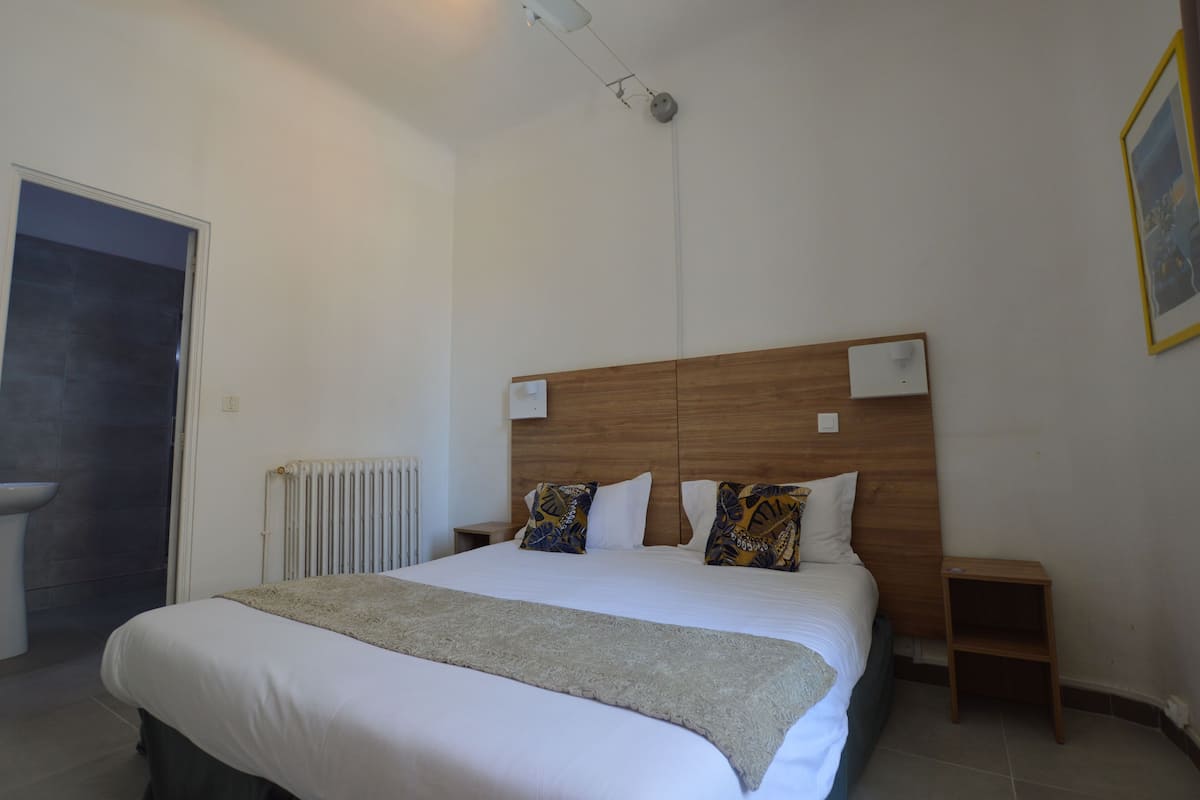 Une chambre à coucher avec un grand lit, une tête de lit en bois, des tables de chevet, un radiateur et une porte.