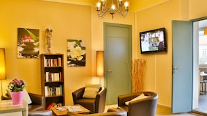 A well-lit living area with a bookshelf, seating, a television, and artwork on the walls.