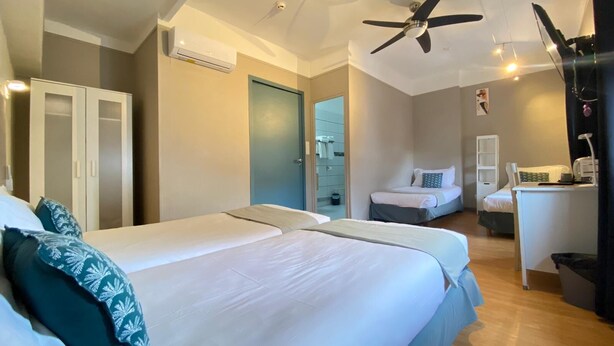 A hotel room with two beds, a desk, a chair, a wardrobe, and a ceiling fan.