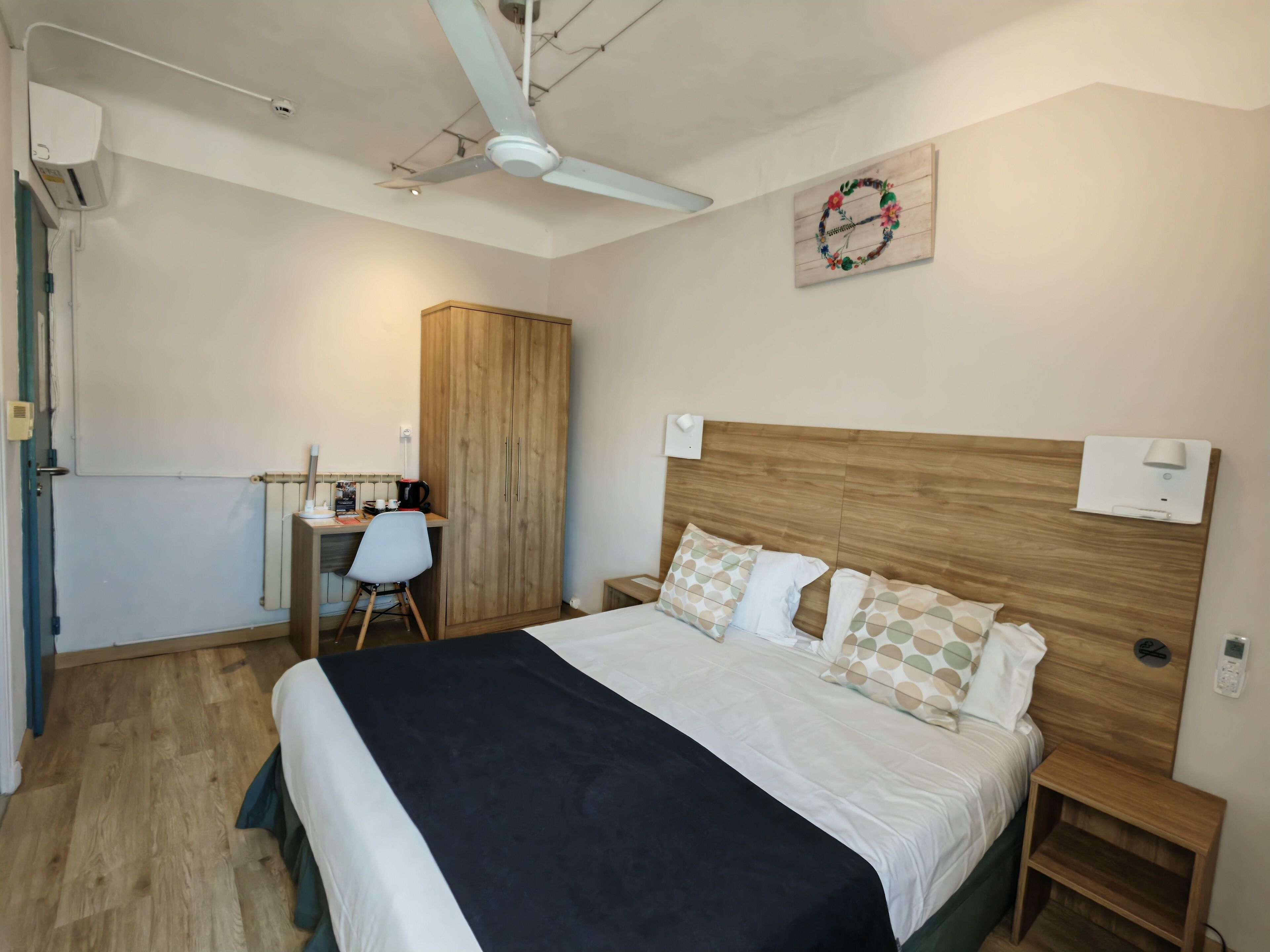 Une chambre à coucher comprenant un lit, des tables de chevet, un bureau, une chaise, une armoire et un ventilateur de plafond.