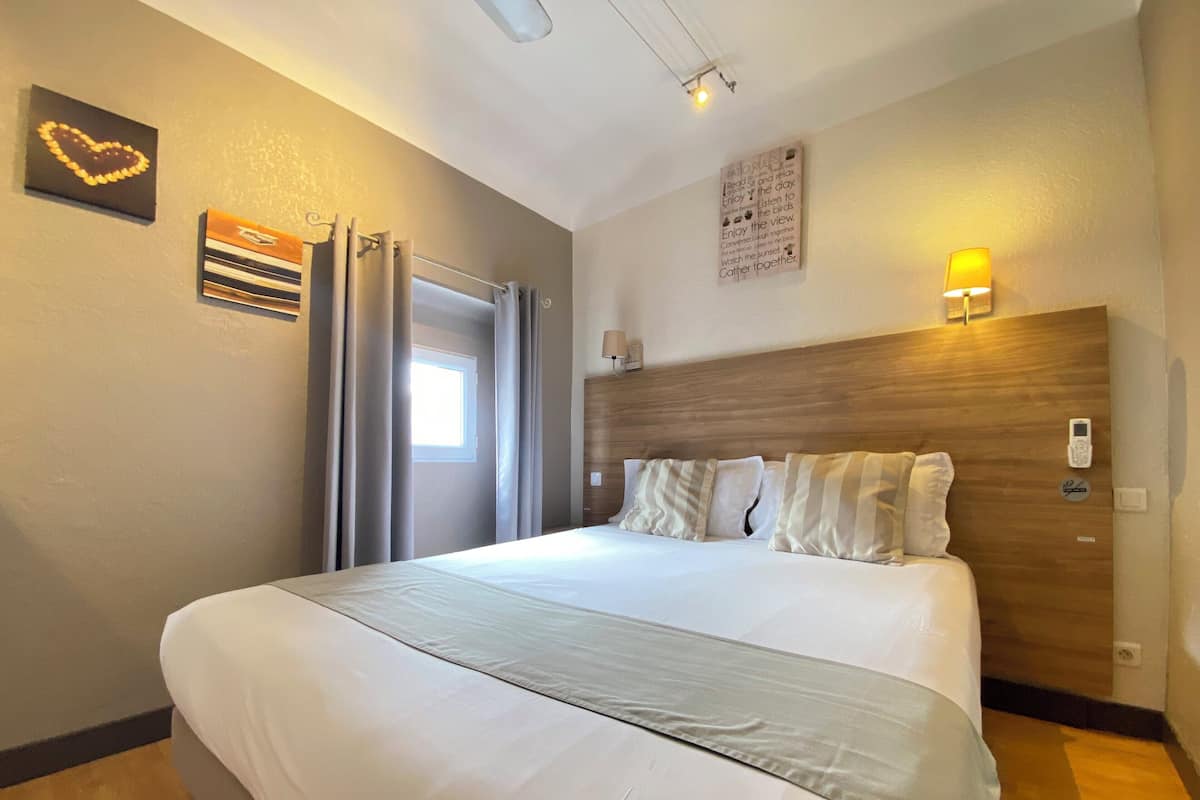 Une chambre d’hôtel moderne avec un grand lit, une tête de lit en bois, une lampe de chevet et un luminaire fixé au mur.