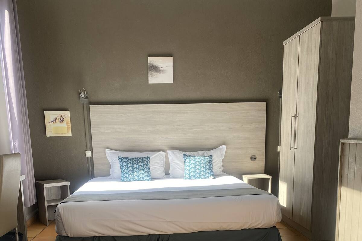 Une chambre d’hôtel avec un grand lit, deux tables de chevet, une armoire et une petite table de chevet avec une lampe.