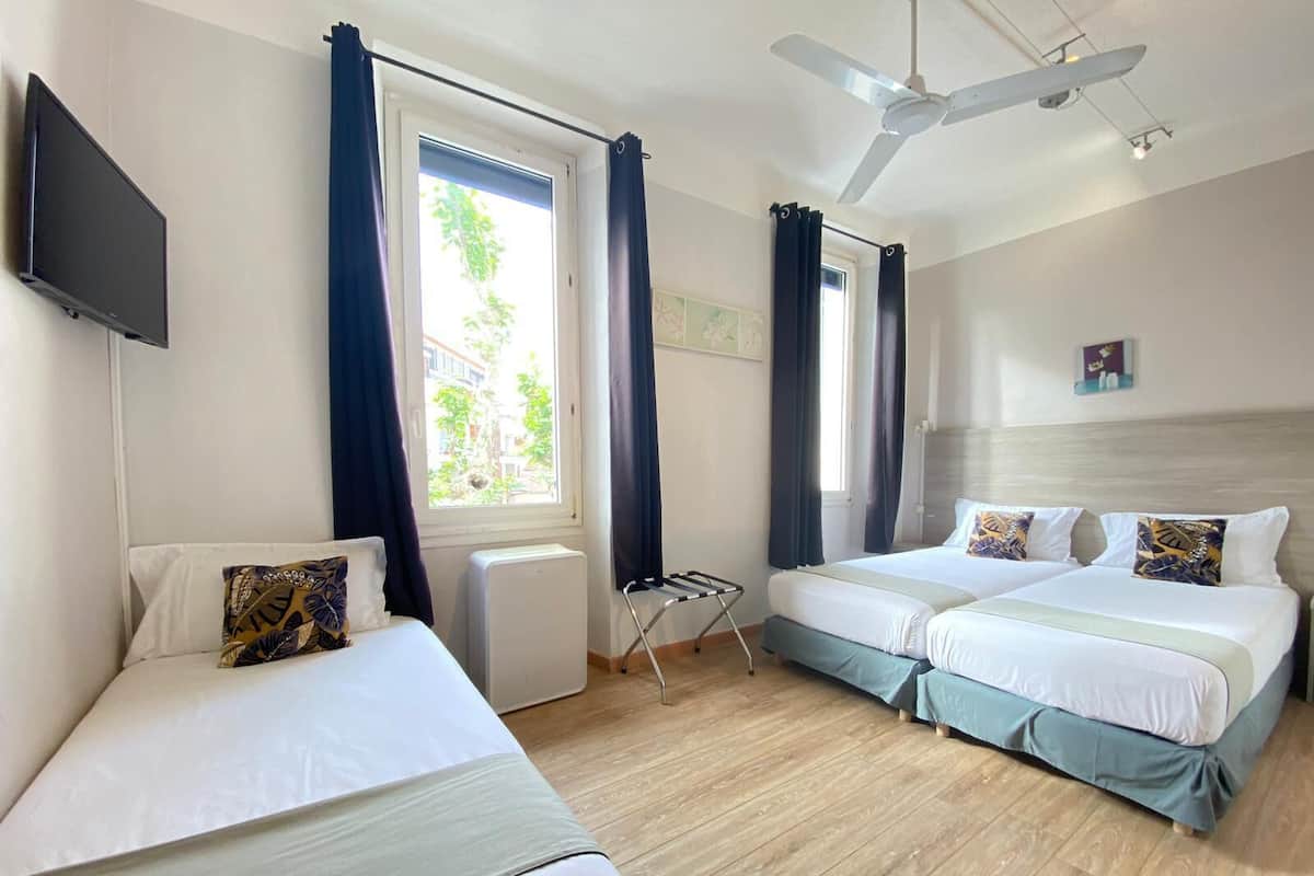 Une chambre d’hôtel avec deux lits, un ventilateur de plafond, un radiateur et une fenêtre avec des rideaux.