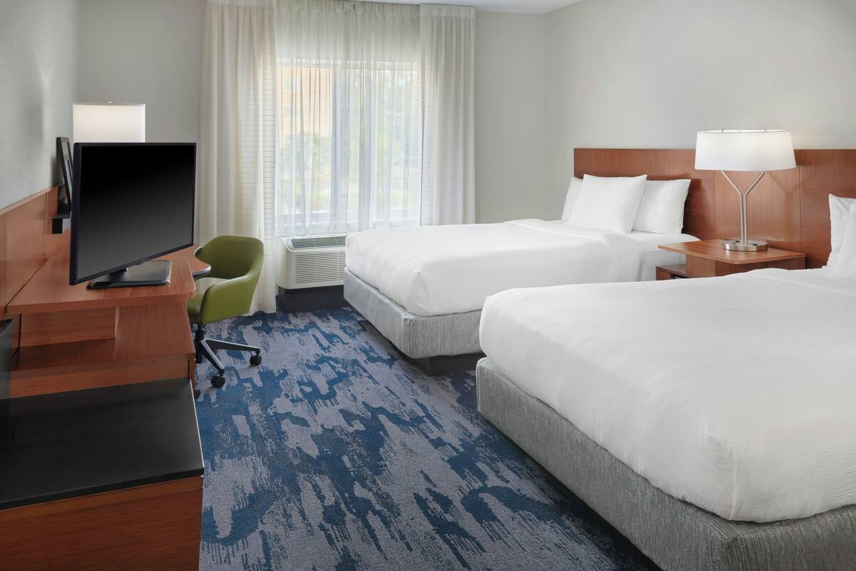 Une chambre d’hôtel avec deux lits, un bureau avec un ordinateur, une chaise et une fenêtre avec des rideaux.