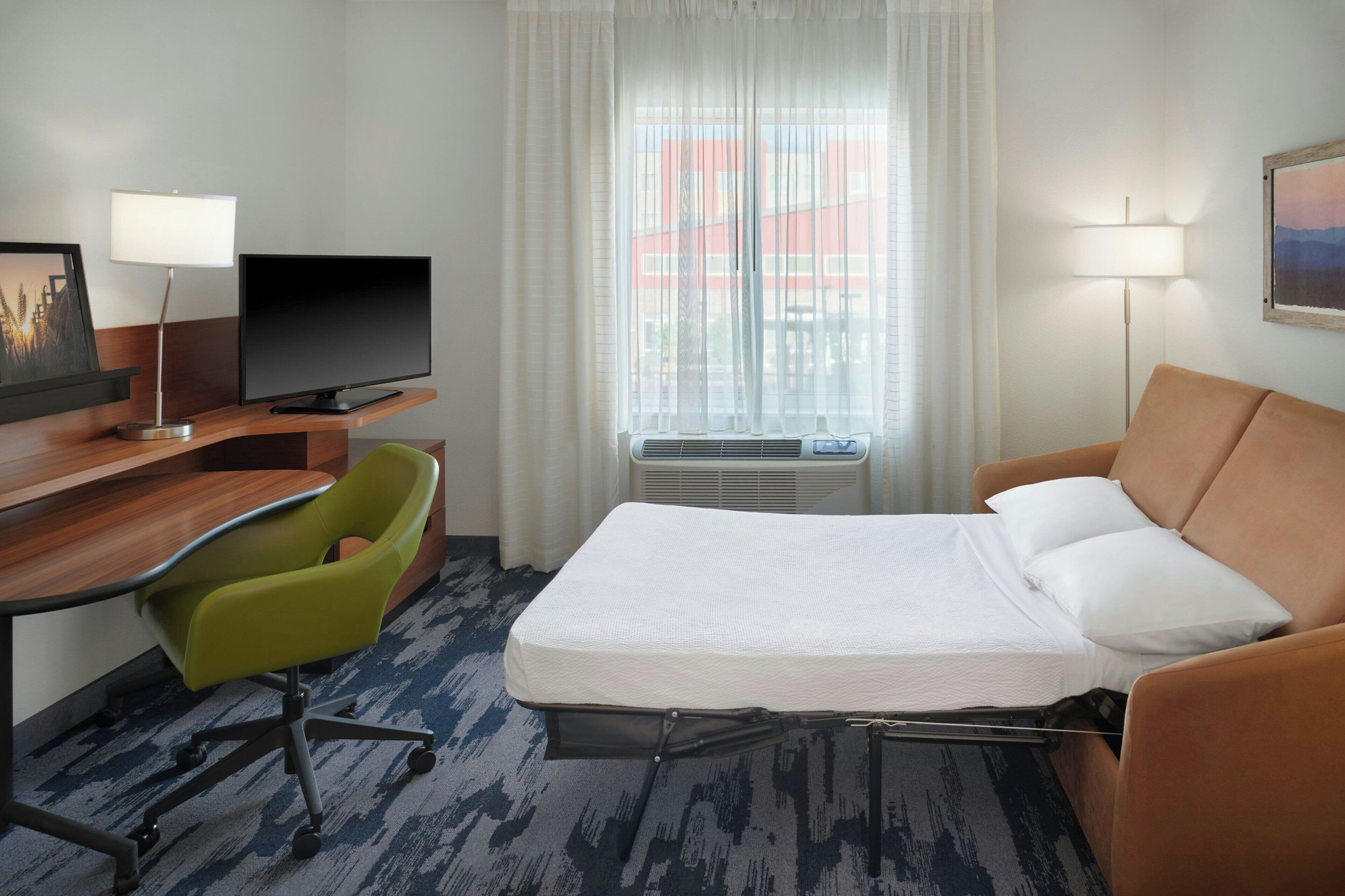 Une chambre d’hôtel équipée d’un lit, d’un bureau, d’une chaise, d’une télévision et d’une fenêtre avec des rideaux.