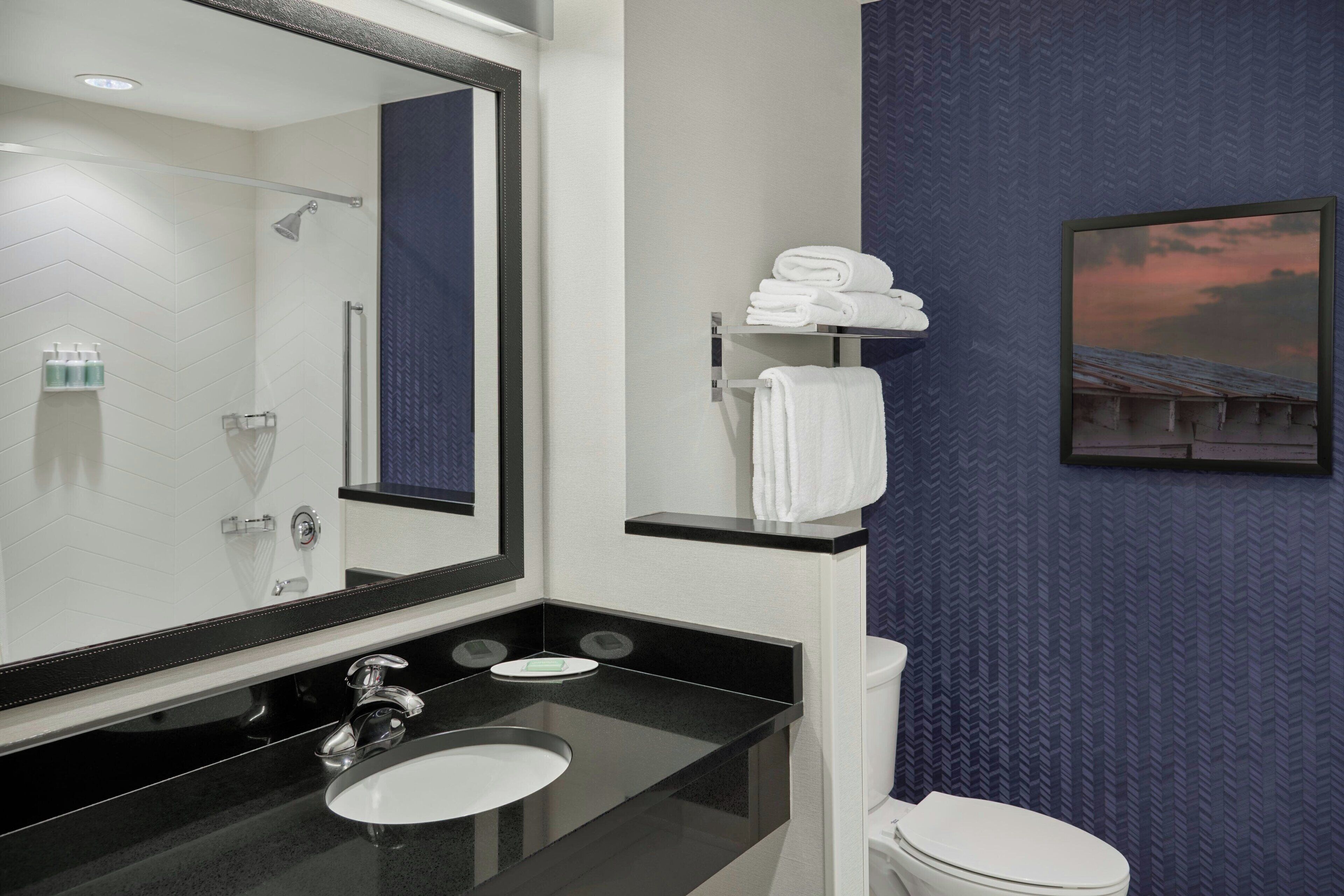 A modern bathroom with a large mirror, black countertop, white sink, and a toilet.