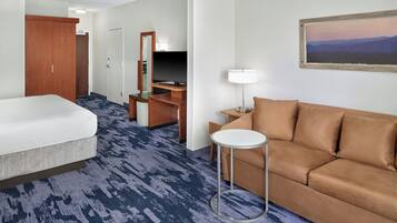 Een hotelkamer met een bed, een slaapbank, een bureau met een lamp, een schilderij aan de muur en een vloerkleed.