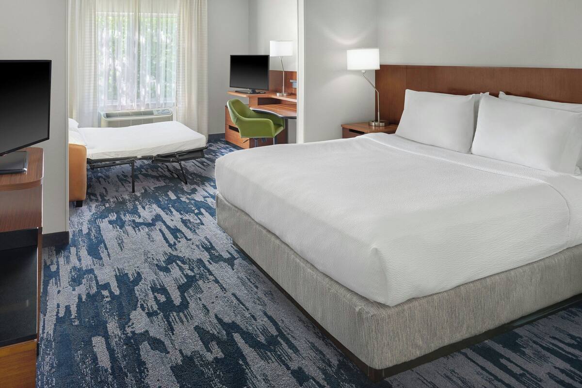 Une chambre d’hôtel avec un grand lit, un bureau avec un ordinateur, une télévision et une chaise.