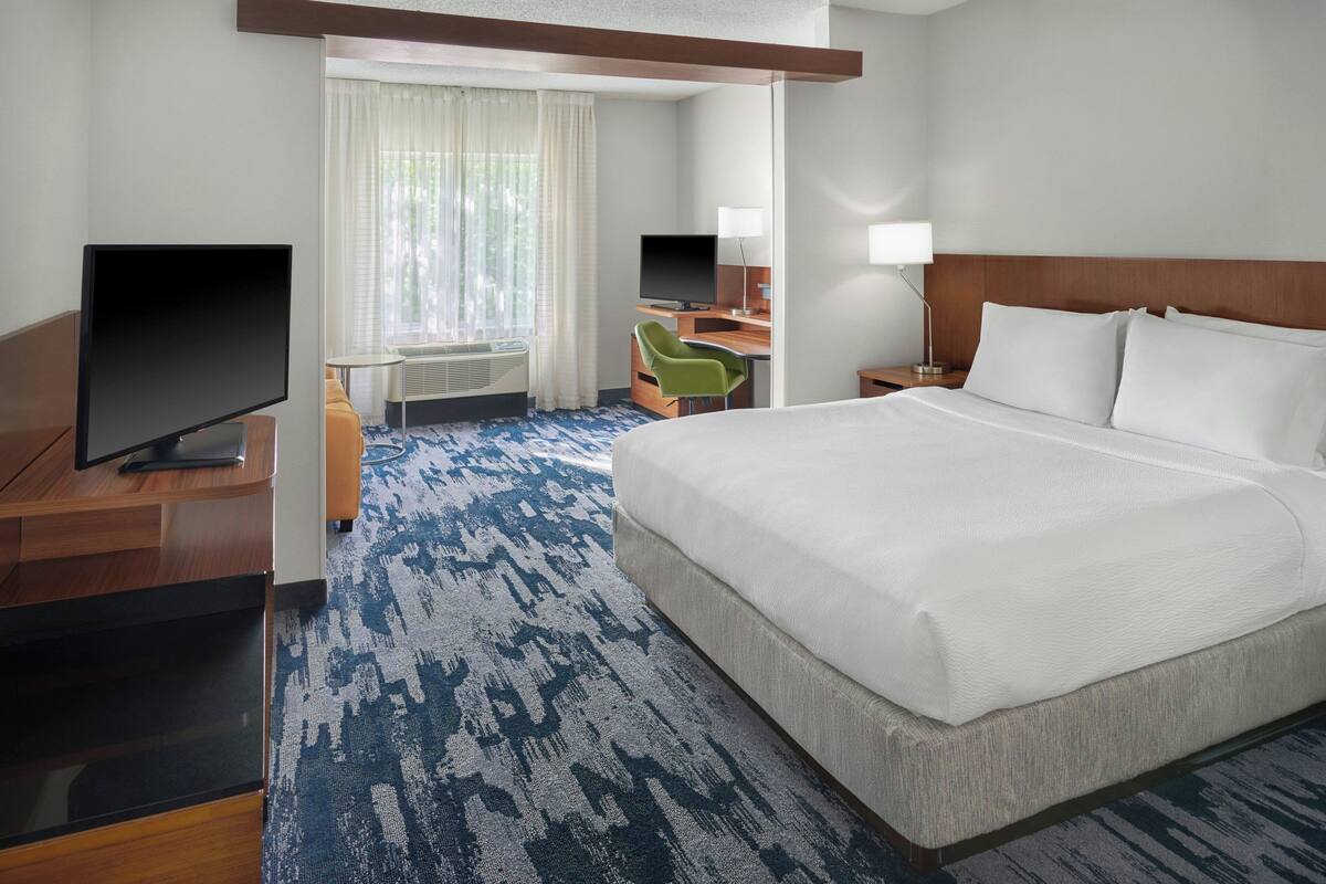 Une chambre d’hôtel avec un grand lit, un bureau avec un ordinateur, une télévision et une chaise.