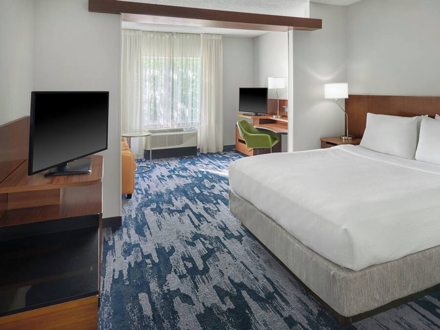 Une chambre d’hôtel avec un grand lit, un bureau avec un ordinateur, une télévision et une chaise.