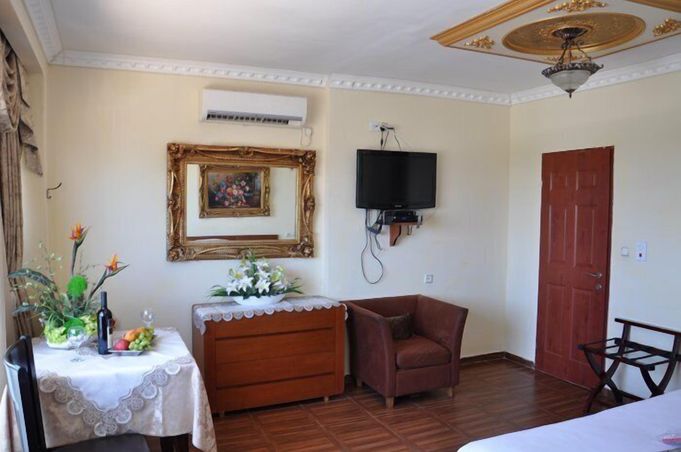 Una habitación con un aparador de madera, un sillón marrón, un televisor montado en la pared y una puerta roja.