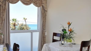 A dining area with a table set for two, a view of the sea through large windows, and a balcony with curtains. - Hotel Bat Yam (Bat Yam)