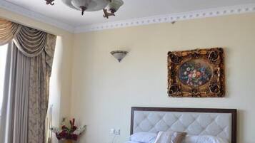 Un dormitorio con una cama grande, una araña, un techo decorativo y un cuadro en la pared.