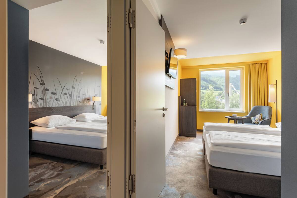Une chambre d’hôtel avec deux lits, une grande fenêtre donnant sur un beau paysage, un bureau et une chaise.